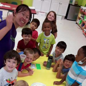 A group of pre-k students and their teacher smile for a photo at snack time