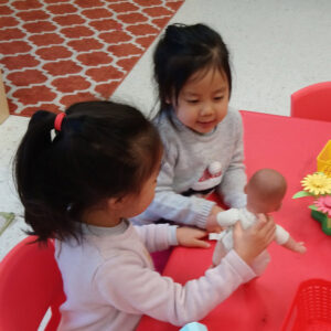 Two preschool girls playing with dolls at a table