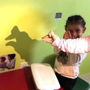 Preschool girl uses a light to make finger puppets on the wall