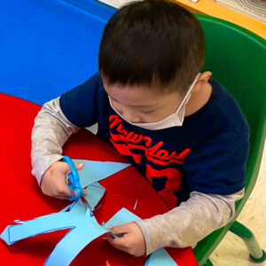 Preschool Boy practices cutting paper with scissors