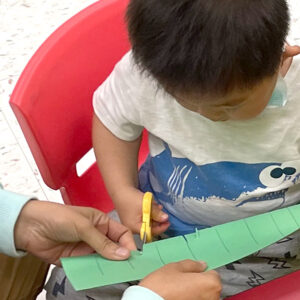 young boy leaning to use scissors