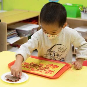 preschool boy making leaf prints with orange paint on construction paper