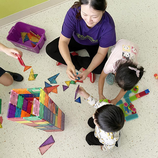 3 children with teacher building a tower out of colorful magnet tiles