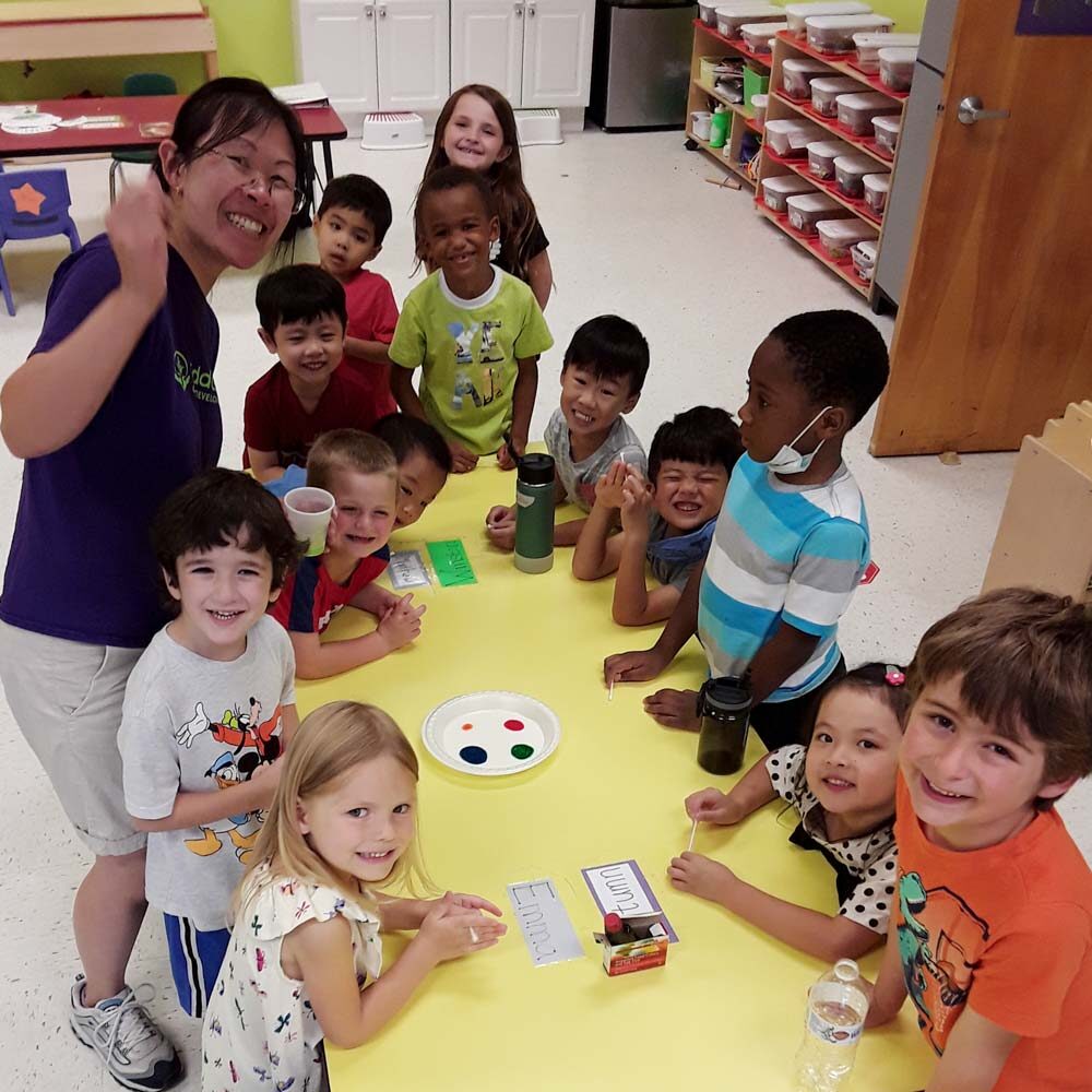 group of pre-k kids - many races, both boys and girls, around a table about to start an art project