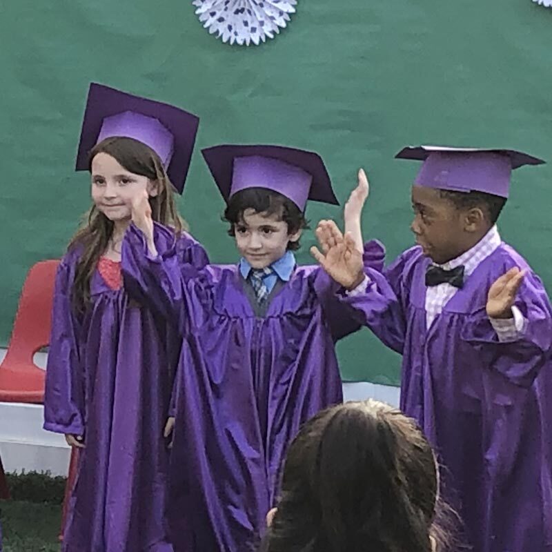 Three 5-year-olds in purple caps and gowns excited about kindergarten