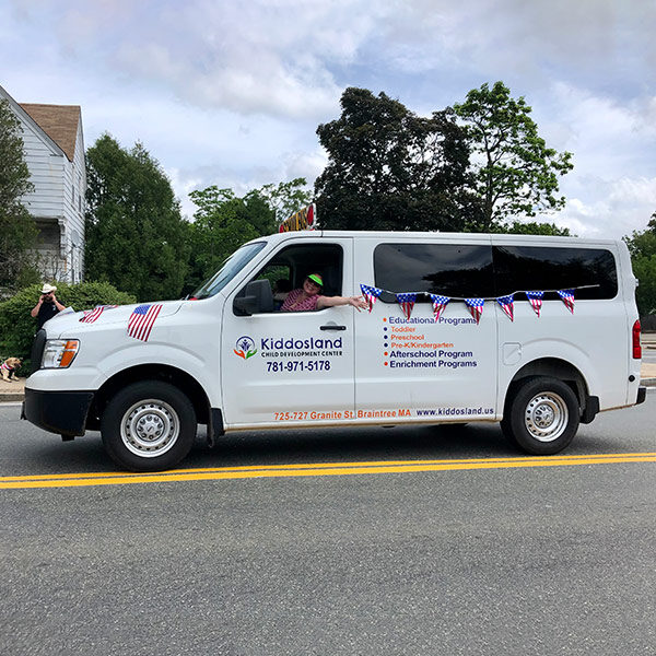Kiddosland Van decorated for holiday parade with flags, smiling driver