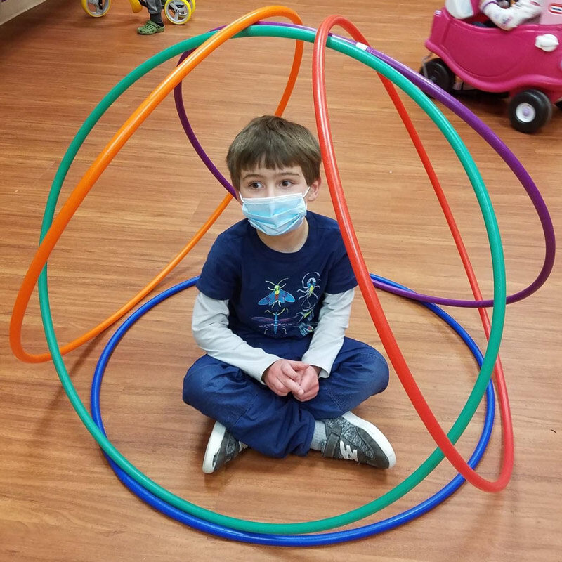 A pre-k boy sits in a cirle of hula hoops.